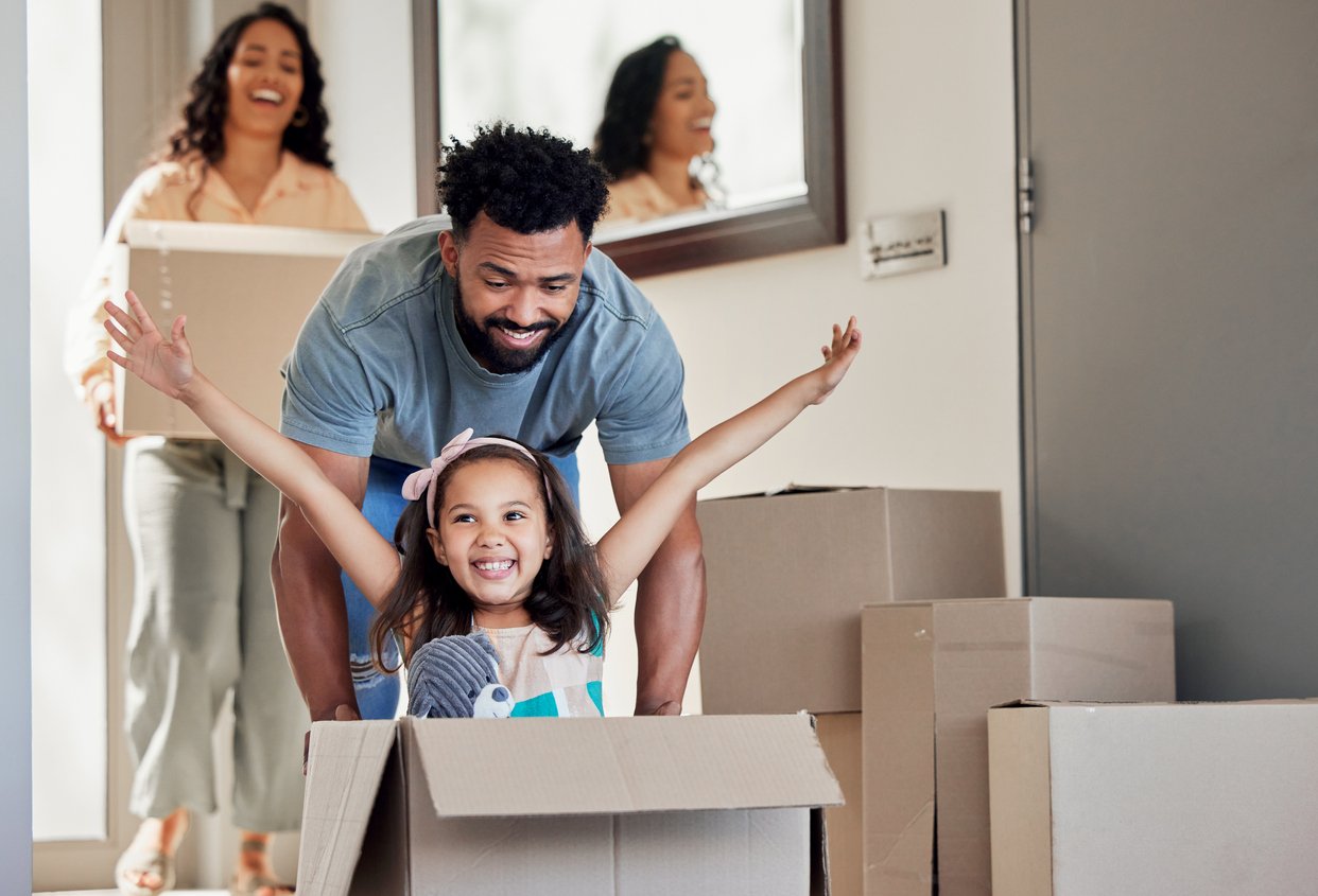 A father pushing his daughter in a box in their manufactured home with the mother behind them